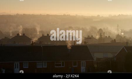 Condensing exhaust from gas-fired central heating rising above rooftops in early morning sunlight over Chesterfield Stock Photo