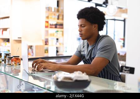 Young male african american owner using laptop at counter in coffee shop. unaltered, cafe culture, people and occupation concept. Stock Photo