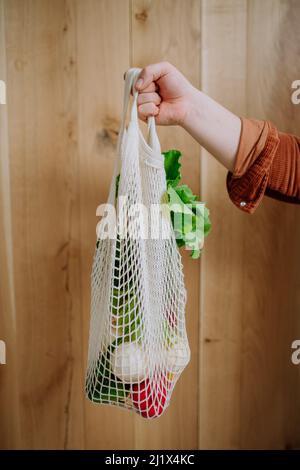 Woman holding a reusable mesh bag with fresh vegetables. Zero waste concept. Stock Photo