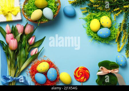 Easter eggs in a basket bouquet of tulips twigs bunny flowers on a blue background. Stock Photo