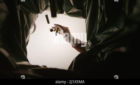 Man putting used batteries in recycling bin in the kitchen. Bottom view from the trash bin. Ecology concept.  Stock Photo