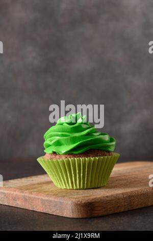 Tasty homemade chocolate cupcake with green whipped cream on brown background. Vertical format. Close up. Stock Photo