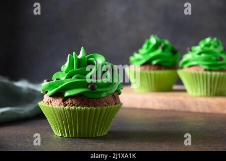 Tasty chocolate cupcakes with green whipped cream on brown background for St. Patrick's Day. Close up. Stock Photo