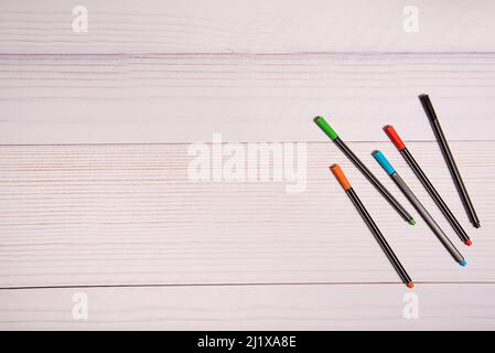 PENS OF DIFFERENT COLORS, ON WHITE WOODEN TABLE. Stock Photo