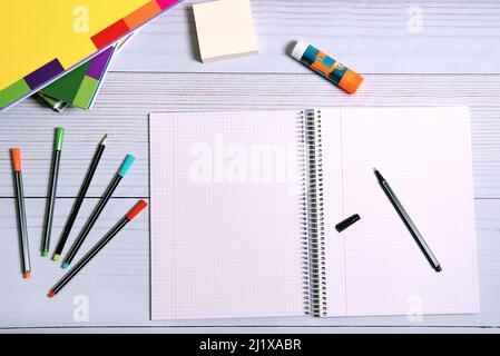SCHOOL SUPPLIES. OPEN CHECKERED NOTEBOOK. OTHER CLOSED NOTEBOOKS, COLORED PENS. Stock Photo