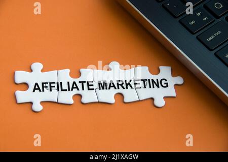 Affiliate marketing text on missing jigsaw puzzle with laptop and brown cover background. Stock Photo