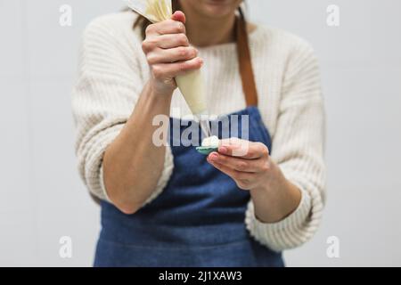 Pastry chef using a pastry bag with cream to fill the macaroons while working in the kitchen. Stock Photo