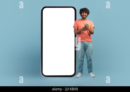 Happy young indian man using cell phone on blue Stock Photo