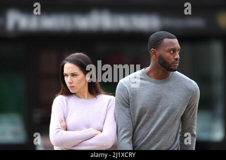 Front view portrait of an angry interracial couple ignoring each other walking in the street Stock Photo