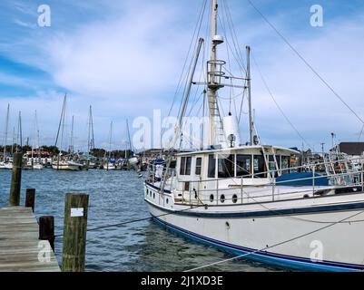 White commercial fishing shrimping boat with mast and rigging is tied to the dock in a marina by ropes. Stock Photo