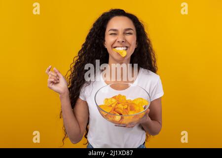Excited Latin Lady Eating Delicious Potato Crisps Stock Photo