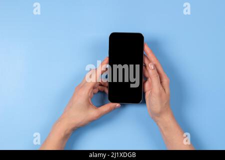 Female hand holding smartphone on light blue background Stock Photo