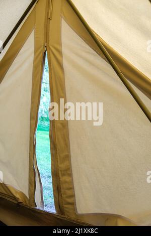 View from inside an old style canvas bell tent at a camp site in a lush green field set up for posh camping also known as glamping. Stock Photo