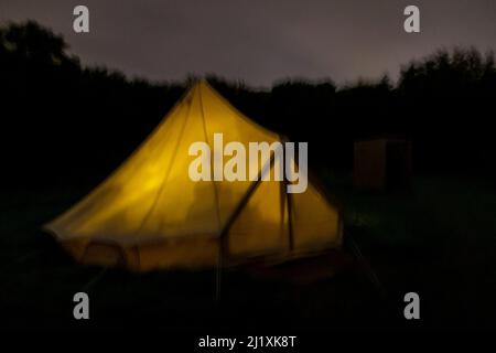 Night time view of a tent glowing from the inside on a glamping, campsite. Stock Photo