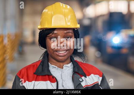 Portrait of African young woman in work helmet and uniform smiling at camera working in factory Stock Photo