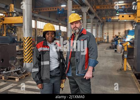 Portrait of couple of workers in uniform smiling at camera while working together at factory Stock Photo