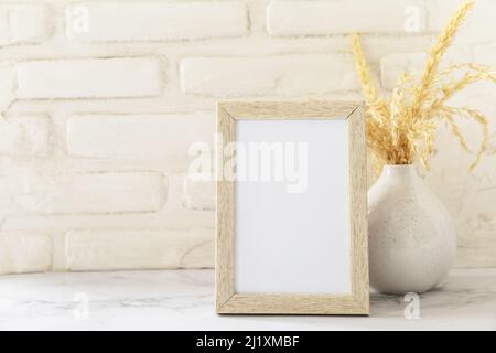 White picture frame mockup. White wall background. Scandinavian interior, neutral color palette with dry grass. Selective focus. Stock Photo