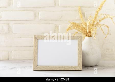 White picture frame mockup. White wall background. Scandinavian interior, neutral color palette with dry grass. Selective focus. Stock Photo
