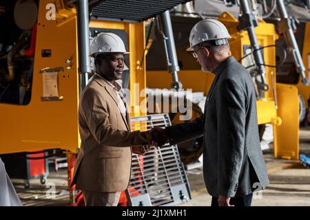 Multiracial engineers in work helmets shaking hands and making a deal during a meeting at an equipment manufacturing plant Stock Photo