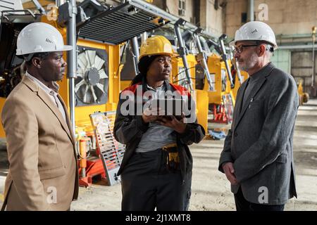 African female foreman using digital tablet in her work during her meeting with engineers in factory Stock Photo