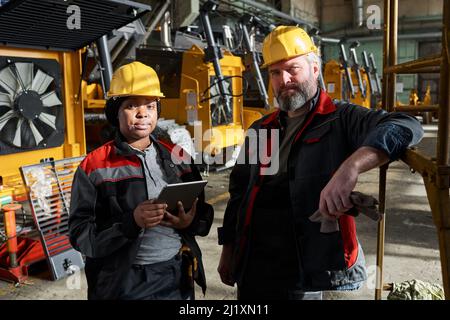 Portrait of couple of technicians looking at camera while standing in warehouse, they controlling the machines with digital tablet Stock Photo