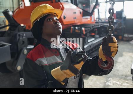 African woman in uniform and work helmet using the control panel to work with crane in warehouse Stock Photo