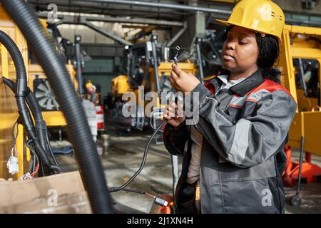 African female worker in uniform connecting wires to equipment during her work in warehouse Stock Photo