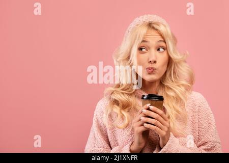 Dreamy young lady holding takeaway coffee and looking aside at empty space on pink studio background Stock Photo