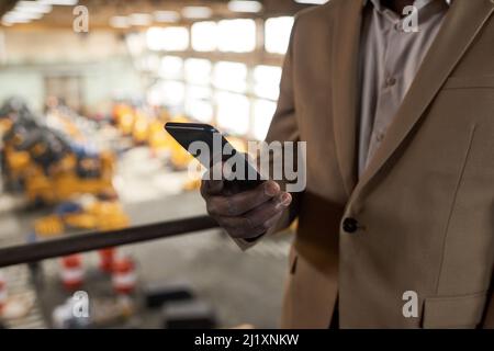 Close-up of businessman in suit typing a message on his mobile phone while working in warehouse Stock Photo
