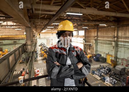 Portrait of African female worker in work helmet and uniform standing on balcony with her arms crossed and looking at camera Stock Photo