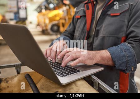 Close-up of engineer in uniform typing on laptop and working online while standing in warehouse Stock Photo