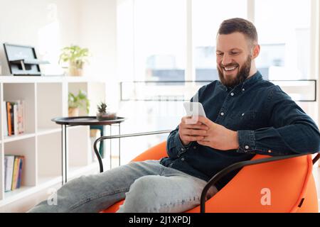 Cheerful Bearded Man Using Mobile Phone Texting Sitting At Home Stock Photo