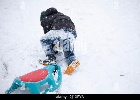 Child in winter. The boy is sledding. A child covered in snow climbs a mountain and pulls a sled behind him. Stock Photo