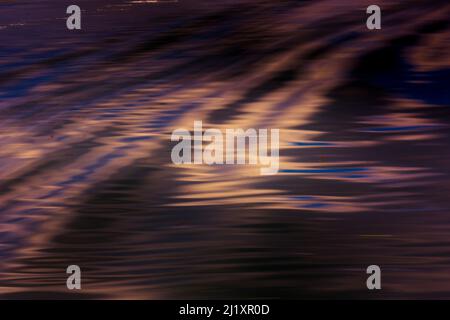 Small waves and ripples reflecting the colourful sky on the surface of a river. Stock Photo