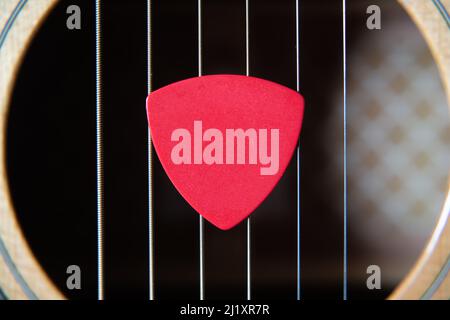 Red guitar pick on an acoustic guitar sound hole Stock Photo