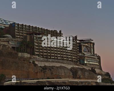 View of large ugly hotel building on the coast of holiday resort Puerto Rico de Gran Canaria, Canary Islands, Spain in the evening with road and rocks. Stock Photo