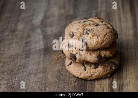 Delicious chocolate cookies on wooden table. Three biscuits with chocolate pieces in stack on wooden surface. Stock Photo