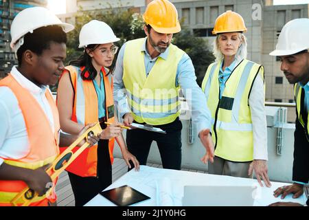 We have a lot to get through. Shot of a diverse group of contractors standing outside together and having a discussion over building plans. Stock Photo