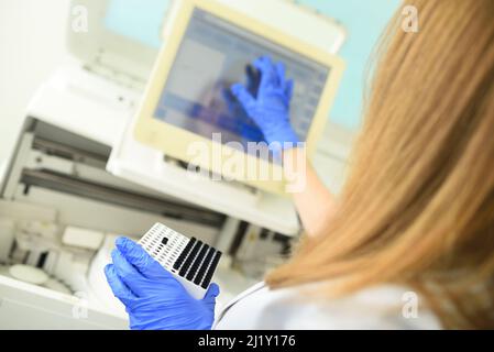 an employee of a medical bacteriological laboratory holds a container with test tubes in his hands against the background of the analyzer. Stock Photo