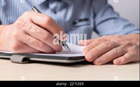 Man sitting at table and writing smth in notebook. Hands closeup. Education, scheduling concept. High quality photo Stock Photo