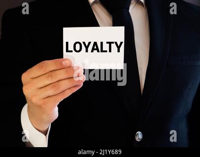 Businessman showing a white card reading - Loyalty - as he withdraws it from the pocket of his suit jacket Stock Photo