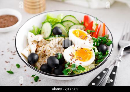 Greek inspired savory oatmeal with fresh cucumber, bell pepper, olives, lettuce, feta cheese, radish sprouts and soft-boiled egg for healthy breakfast Stock Photo