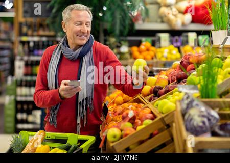 Smiling man using cell phone while shopping at supermarket Stock Photo