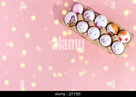 White Easter eggs with various cheerful and sad painted faces and a painted bunny are placed in the corner of the image on a pink background. Brilliant yellow rays. Top view, copy space. Stock Photo