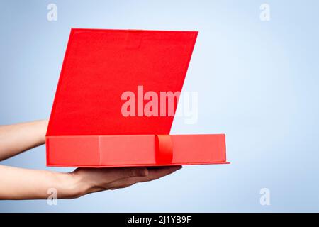 Female hands opening red elegant luxury box with ribbon. Mockup present gift box on light blue background. Front view Stock Photo