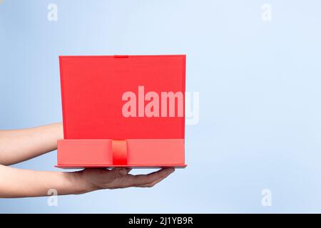 Female hands opening red elegant luxury box with ribbon. Mockup present gift box on light blue background. Front view Stock Photo
