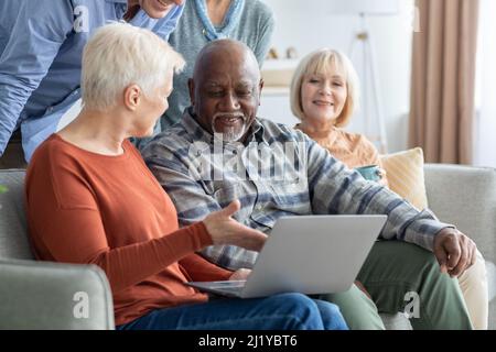 Cheerful elderly people spending time together at home, using laptop Stock Photo