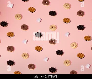Bright fresh sweets summer pattern of chocolate waffles, vanilla donuts and sweet candy on minimal pink background. Stock Photo