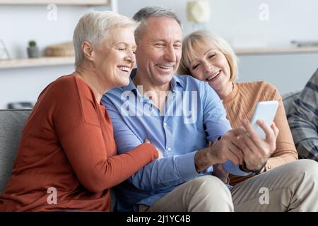 Positive senior man and women sitting on couch, taking selfie Stock Photo