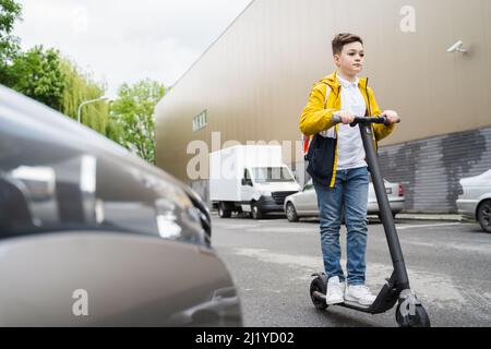 Modern schoolboy with a backpack on his shoulders rides on electric scooter around the city Stock Photo